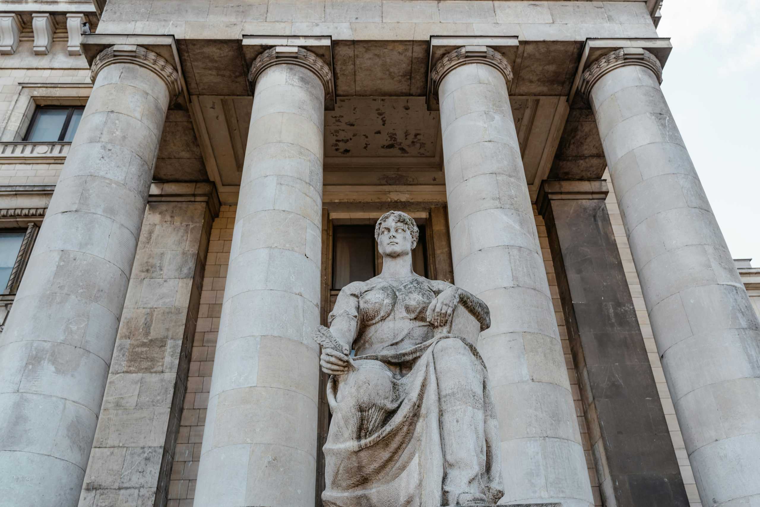 Majestic neoclassical building facade with statue and pillars, photographed in daylight.