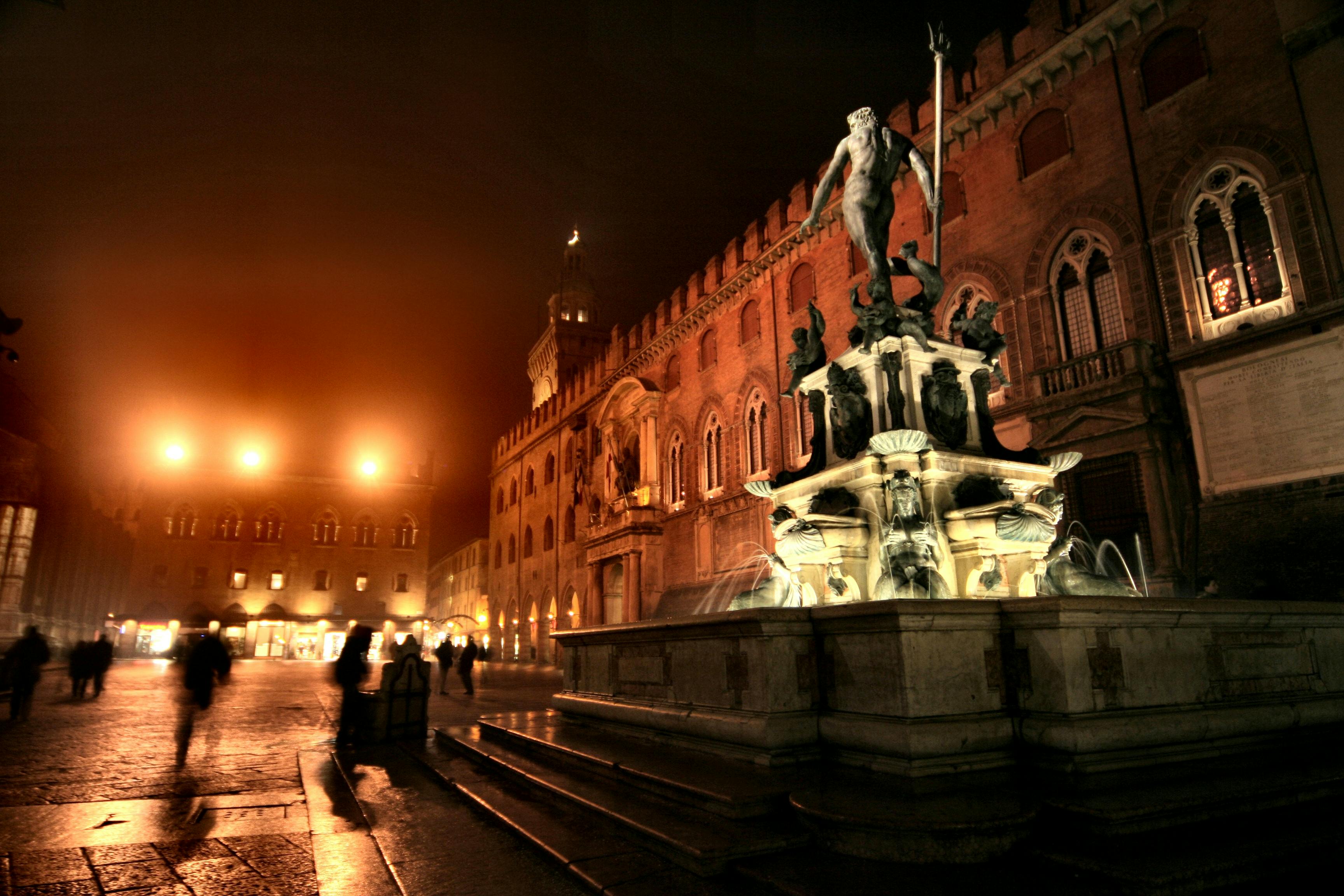 Captivating night view of the Neptune Fountain illuminated in Bologna, Italy, showcasing historic architecture.